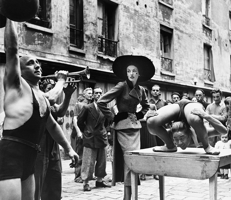 Elise Daniels entourée d’acrobates de rue, ensemble par Balenciaga, Le Marais, Paris, 1948. Photographie de Richard Avedon © The Richard Avedon Foundation